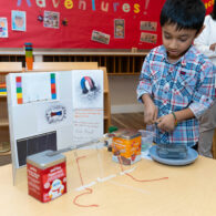 Elementary age child at Montessori school demonstrating his science fair project on a table