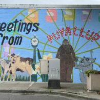 Mural that says "Greetings from Puyallup" with cows, flowers and Big Foot on it.