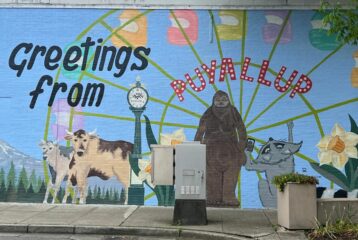Mural that says "Greetings from Puyallup" with cows, flowers and Big Foot on it.