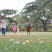 Happy group of diverse cute little children hunting Easter eggs, wearing bunny ears. kids holding basket, running to collect eggs on grass while playing outdoors at park