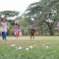 Happy group of diverse cute little children hunting Easter eggs, wearing bunny ears. kids holding basket, running to collect eggs on grass while playing outdoors at park