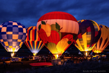 Four huge hot air balloons, glowing from lights within against a night sky