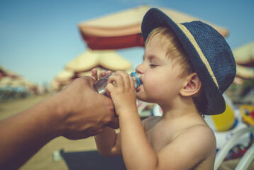 Adult helping child stay hydrated by offering a drink of water during hot weather.