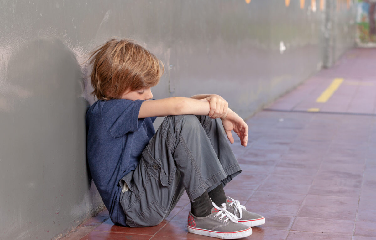 Student sits slumped against school hallway wall, looking down