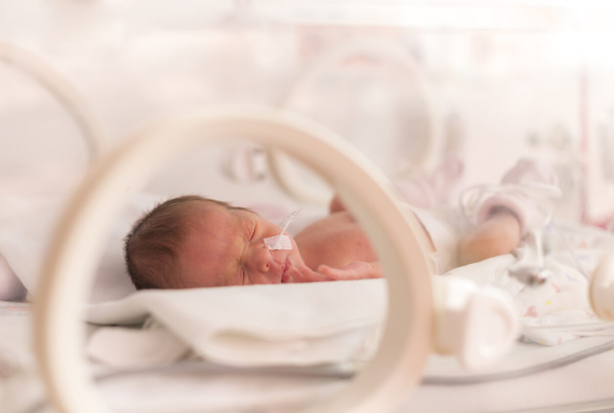 Newborn baby lying in a hospital NICU bed with monitoring equipment