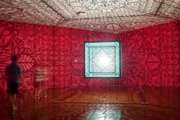 Laser-cut steel cube by Anila Quayyum Agha, suspended from the ceiling and casting shadows.