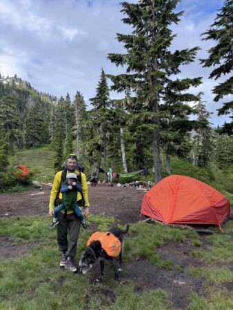 Family posing in front of campsite, parent wearing Trail Magik carrier