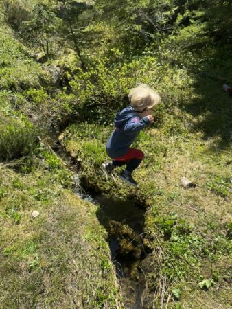 Child jumping over a creek on a mountain trail