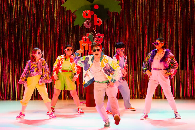 Cast members in colorful jackets and sunglasses dance in front of a glitter curtain in Chicka Chicka Boom Boom: The Musical at Seattle Children’s Theatre.