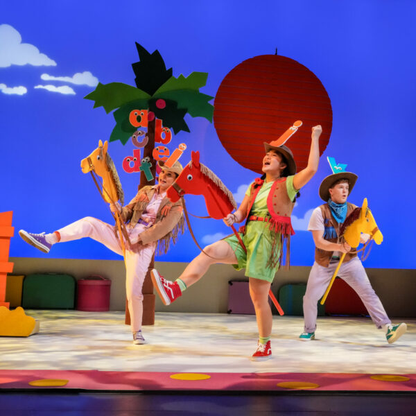 Three actors dressed as letters perform a lively rodeo scene with hobby horses in Chicka Chicka Boom Boom: The Musical at Seattle Children’s Theatre.