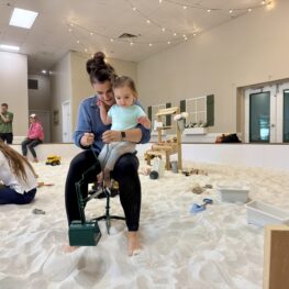Mother and toddler sitting together on a toy digger inside SandGarden’s indoor sandbox in Issaquah