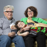 Alex Butler, creator of Taco vs Burrito, sits with his parents Leslie Pierson and Jeff Butler at their Seattle home — the family whose support and creativity turned a kitchen-table idea into a nationwide hit.