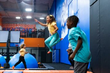 Kids jumping on trampolines at an indoor Sky Zone park with padded walls and bright play features.