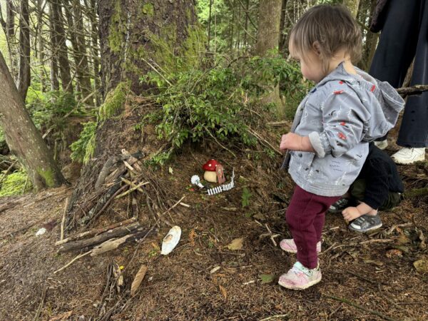 Toddler exploring the Gnome Trail in Seabrook, Washington, looking at tiny gnome houses and decorations along a forest path covered in fall leaves.