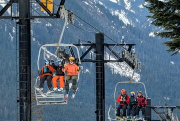 Families riding a chairlift at the Summit at Snoqualmie on a winter day, with skiers and snowboarders bundled in colorful gear and the snow-covered Cascade Mountains rising behind them.