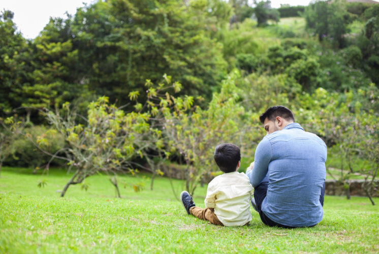 dad latin man in jean shirt enjoys his beautiful garden playing with little son in yellow shirt and beautiful sunny day